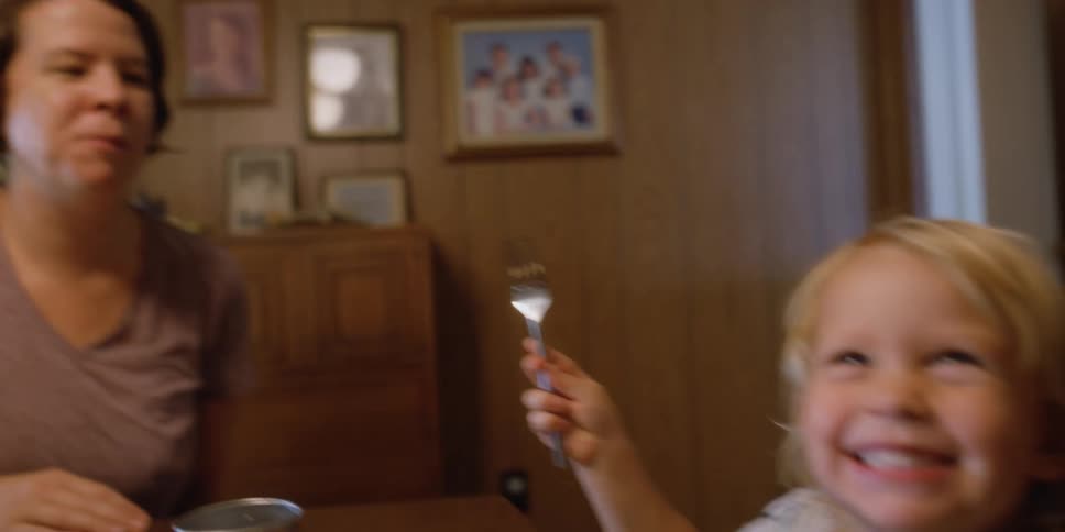 A little girl sitting on a chair at a table feeding a woman with a fork