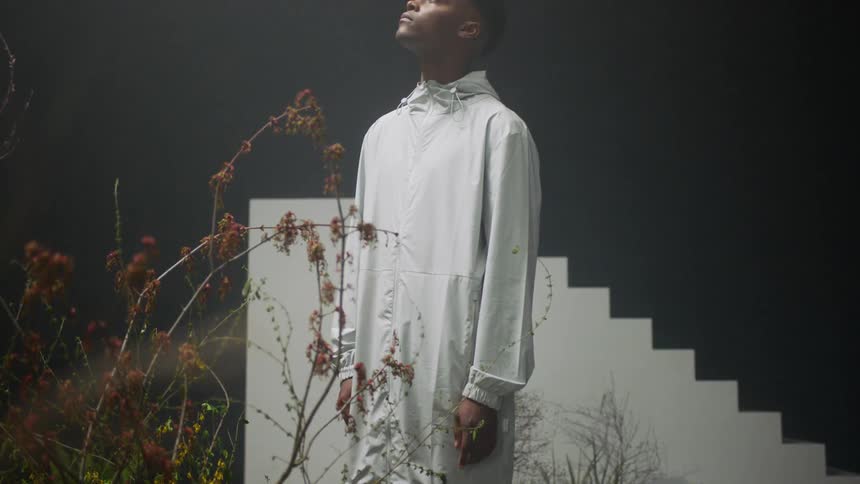 A man stands near plants and a white staircase while looking up