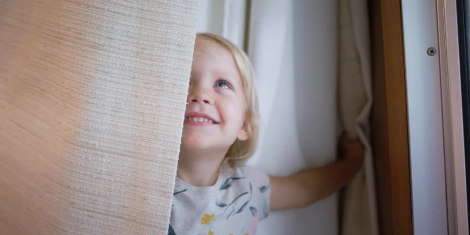 Girl playing peek a boo under the curtains at home