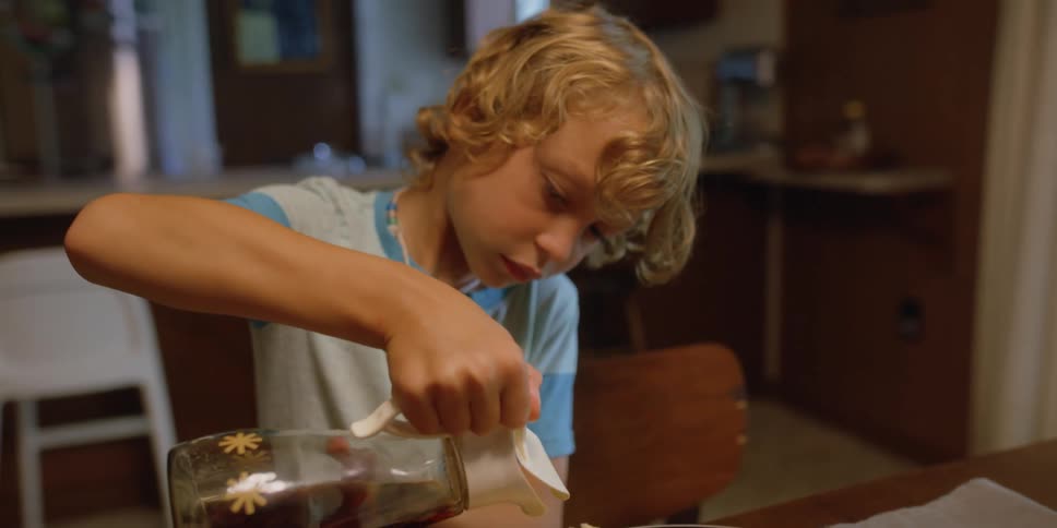 A boy pours syrup into a plate of breakfast food at a home table