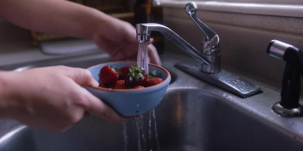 A woman stands in front of her kitchen sink and washes strawberries