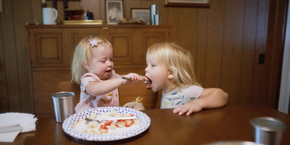 Girl feeding spoonfuls of juice to her sister on the dinner table at home