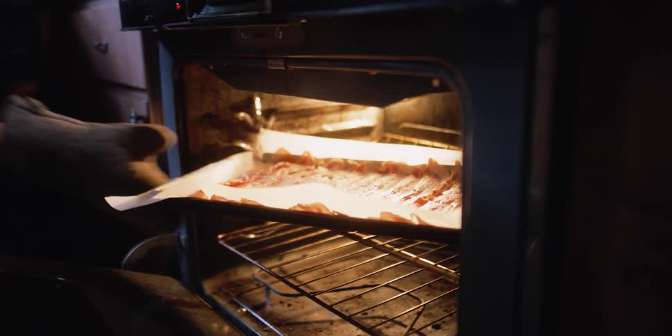 Woman placing a baking tray inside an oven at home