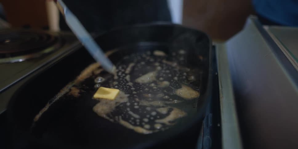 A person is placing butter on a hot griddle and moving it around to melt