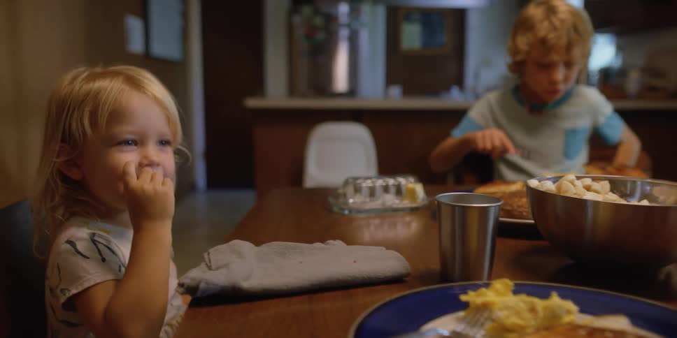 A person pours syrup on to a plate of food and passes it to a young girl at the table
