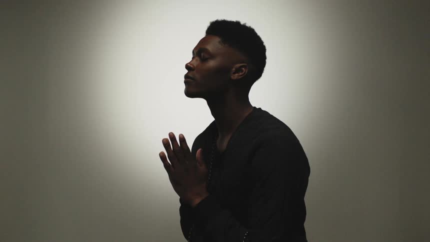 A man in a room praying with a wall in the background