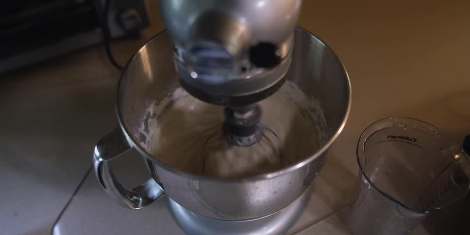 A mixing bowl is on and mixing a batter on top of a counter
