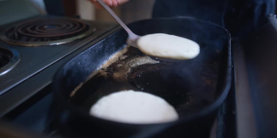 Woman cooking pancakes over a hot pan on a kitchen range at home