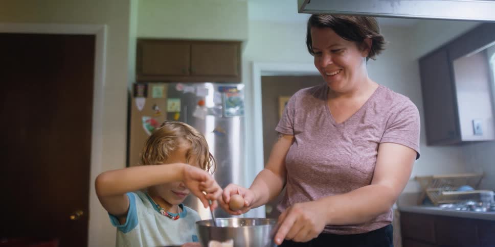Mother and child stir eggs into mixture in metal bowl