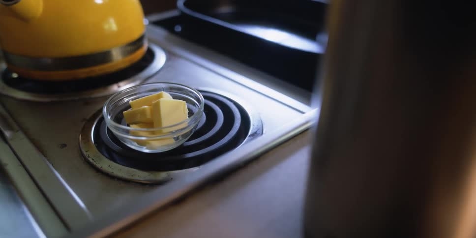 A person setting a bowl of butter on a stove