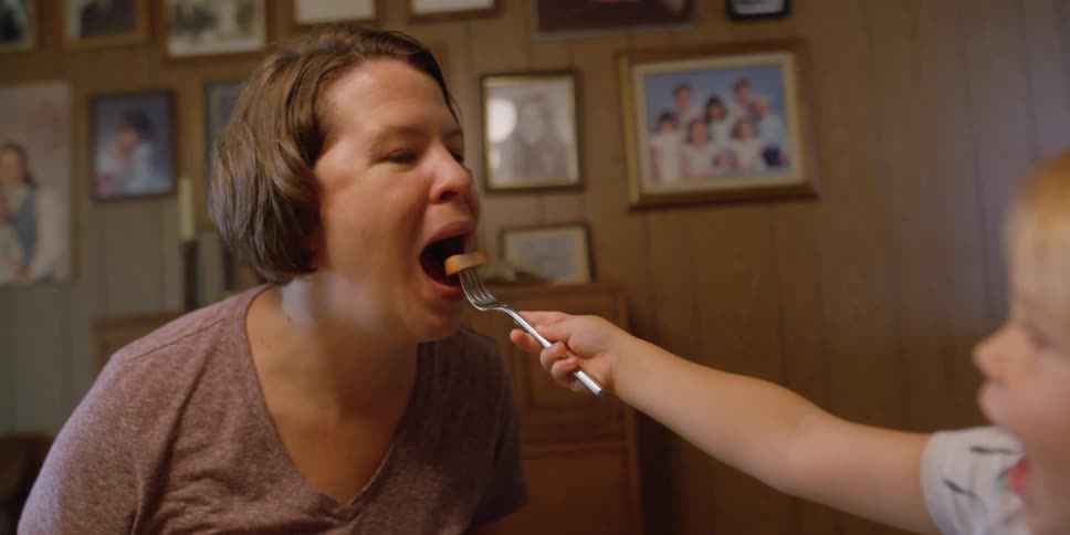 A daughter is feeding her mother food at the dinner table