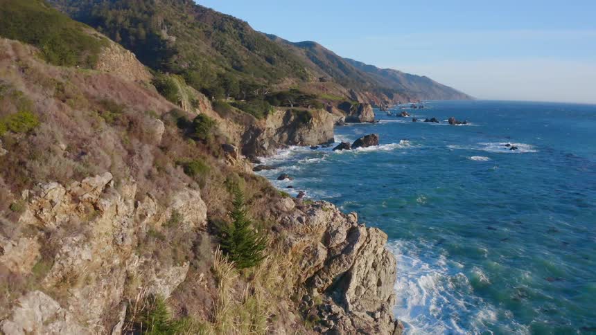 Ocean waves splash as they hit the rocks near the mountains