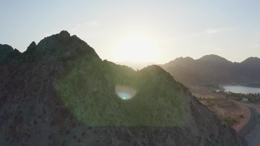 Sun peaks over mountain near road leading past buildings sitting near lakes