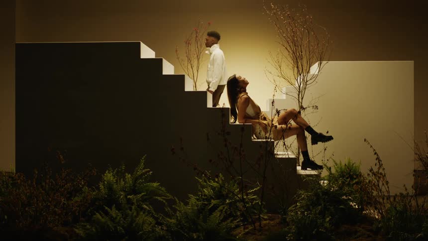 Models sitting and walking over stairs in a stage surrounded by vegetation