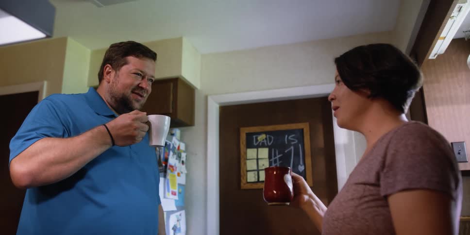 A man and woman stand in front of each other talking and drinking from small mugs