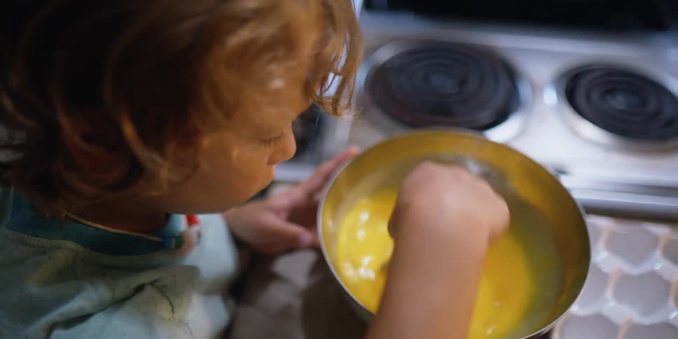 Curly hair boy stirs eggs in the bowl in the kitchen