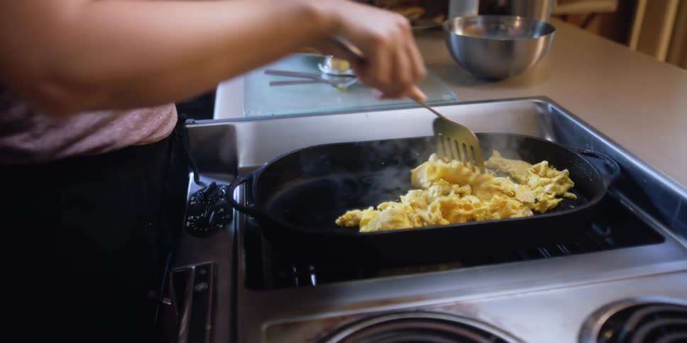 A woman is cooking eggs on an oven indoors