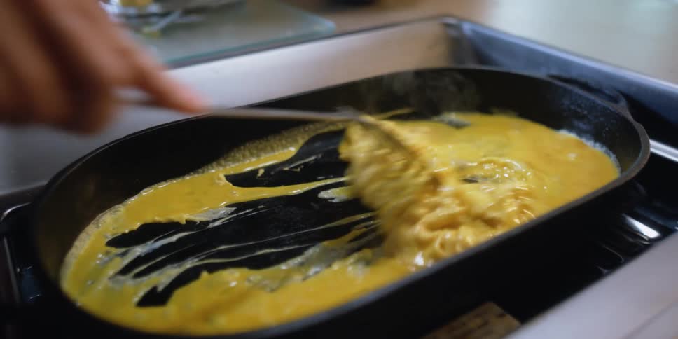 A person stirs eggs cooking in a pan