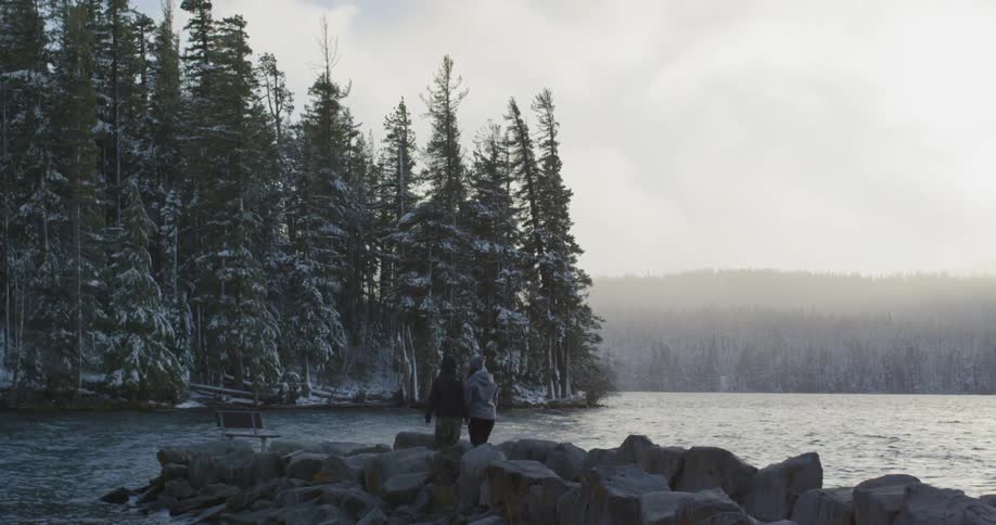 Two women walk down a jetty and overlook a lake on a cold winter day