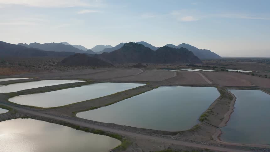A landscape with ponds with a mountain range the sky and clouds in the background
