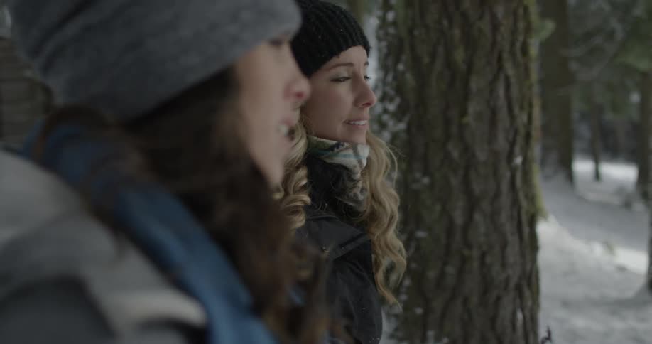 Two women sit talking in amidst pine trees and snow