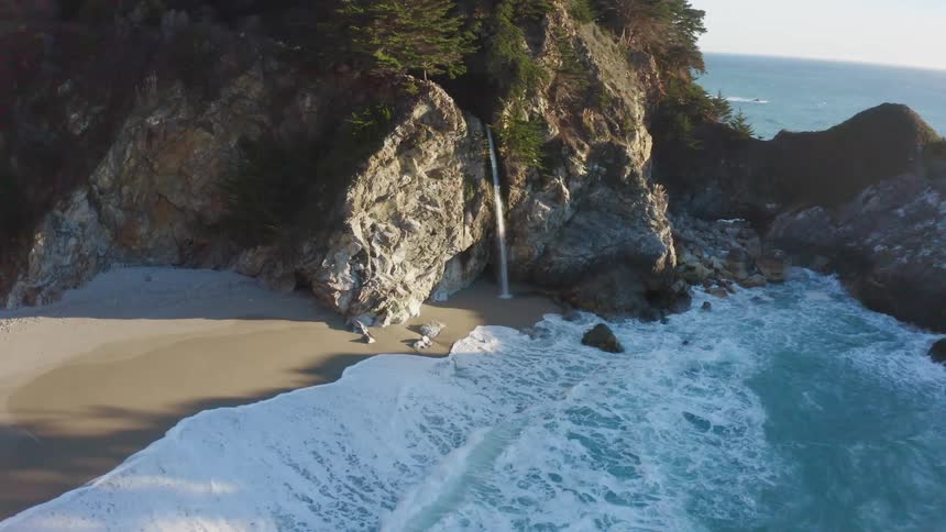 Water flows down onto the beach from the rocky cliff as waves break and splash on shore