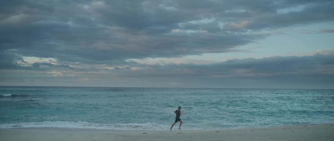 A person can be seen running along a beach in front of crashing ocean waves