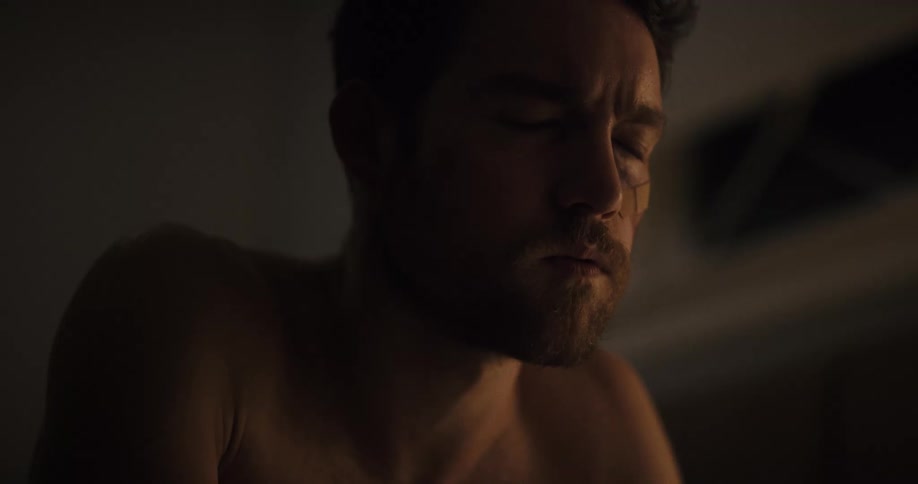 Angry worried shirtless young man ends a call on his phone inside a dimly lit room