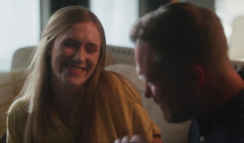 A young woman reads a letter and cheers before being congratulated with a hug by a man sitting beside her