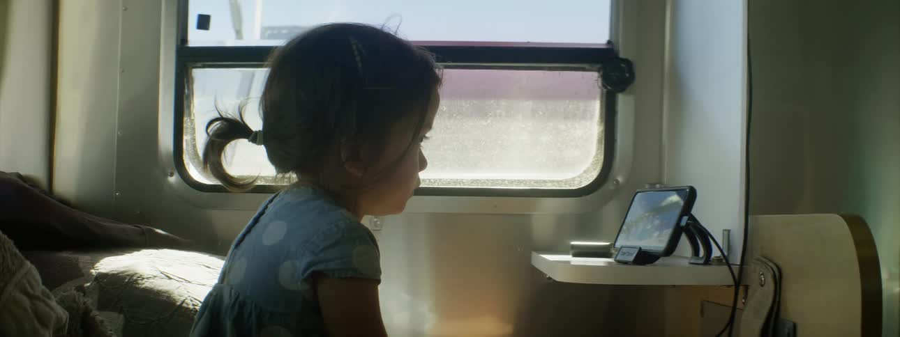 A girl in a room looking at a tablet with a wall and window in the background