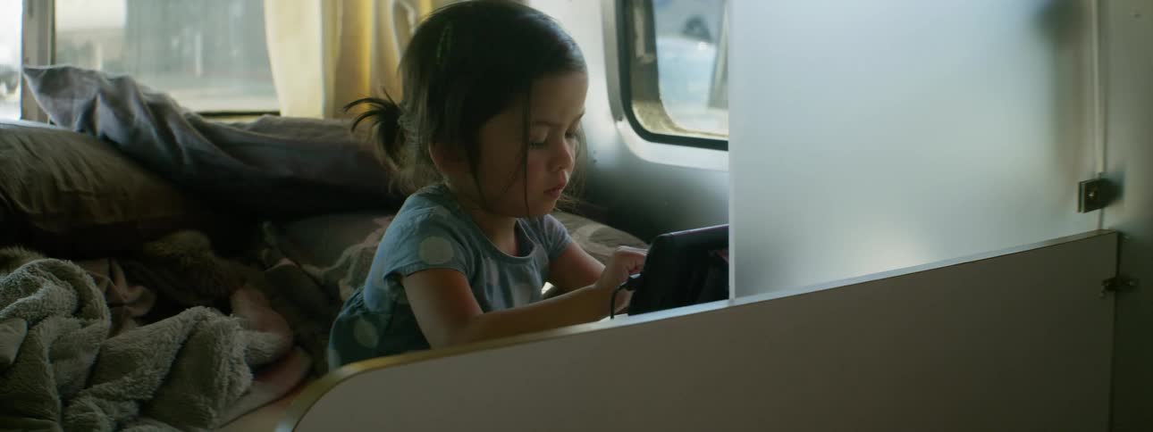 Toddler resting in bed uses her fingers on the touchscreen of a tablet