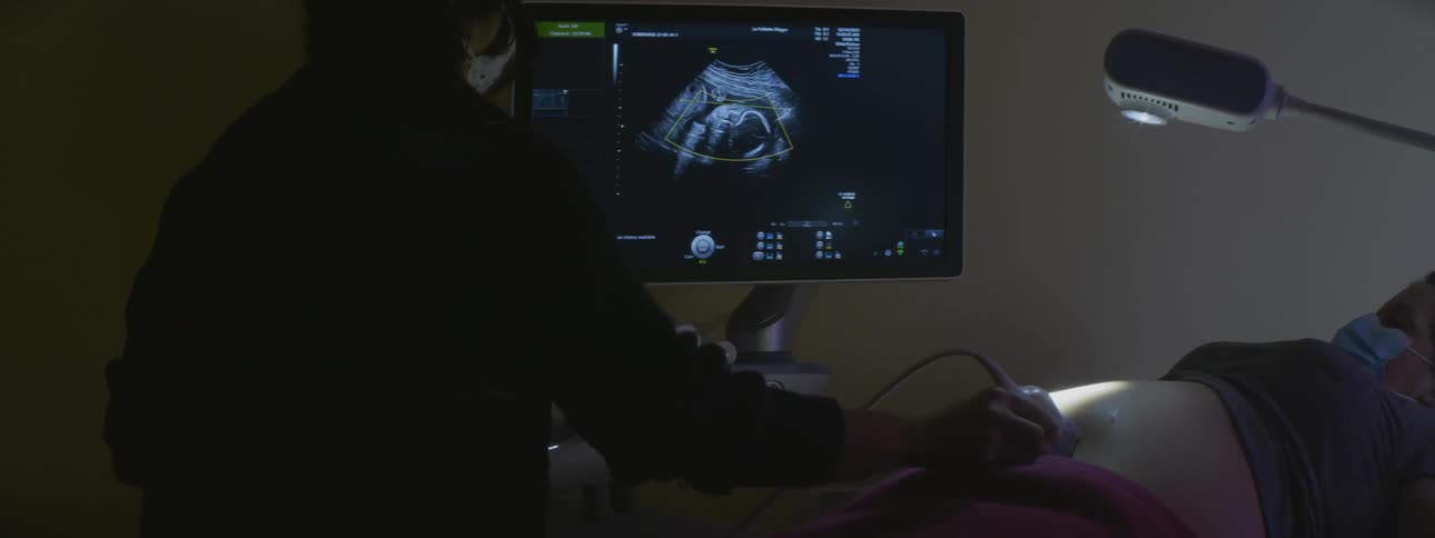 A woman is getting an ultrasound of her pregnant belly done in a dark room