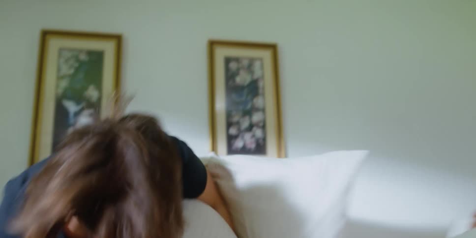 A man woman and little boy engage in a pillow fight in a bedroom during the day