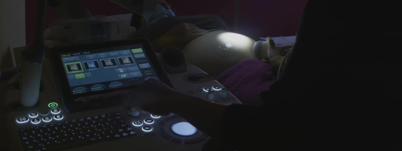 A technician adjusts dials on a machine as they perform an ultrasound on a pregnant woman