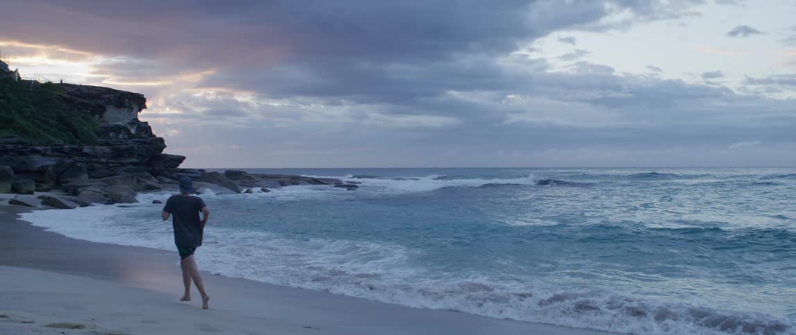 A man running down the edge of a beach at sunset