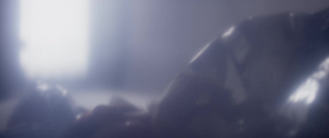 A woman in a room laying on a bed with a thermal blanket with a window and a wall in the background