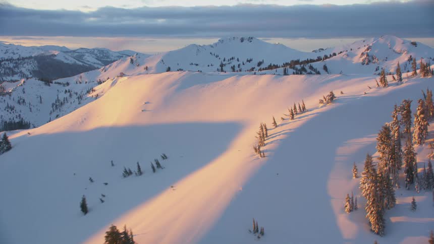 A range of mountains are coated in thick snow and dotted with tall evergreen trees