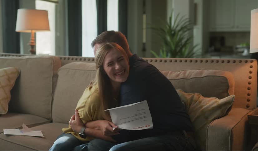 Couple sitting in a couch at home celebrate after opening and reading a letter