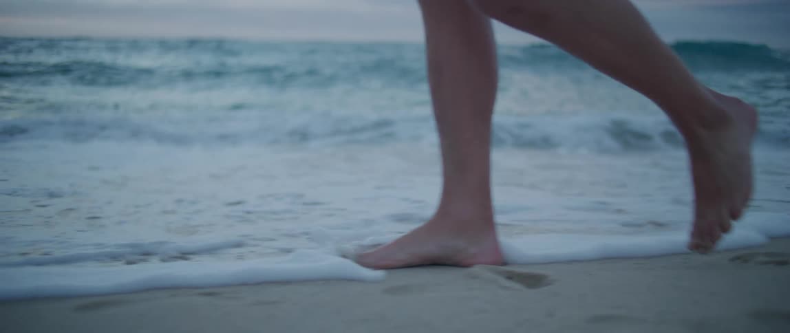 Someone with bare feet walking across a beach as the waves roll over their feet