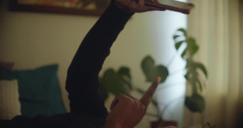 A woman lays on the bed and holds her cell phone in the air having a video call