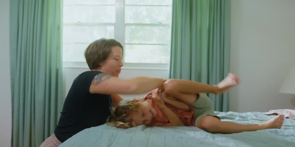 Mother playfuly tickling her son over the bed at home