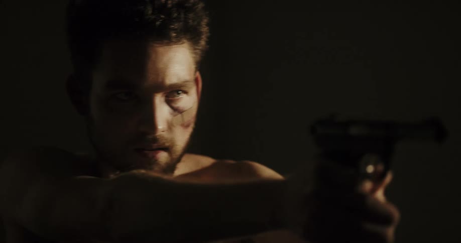 A man spins around quickly and points a black gun standing inside of a dark room