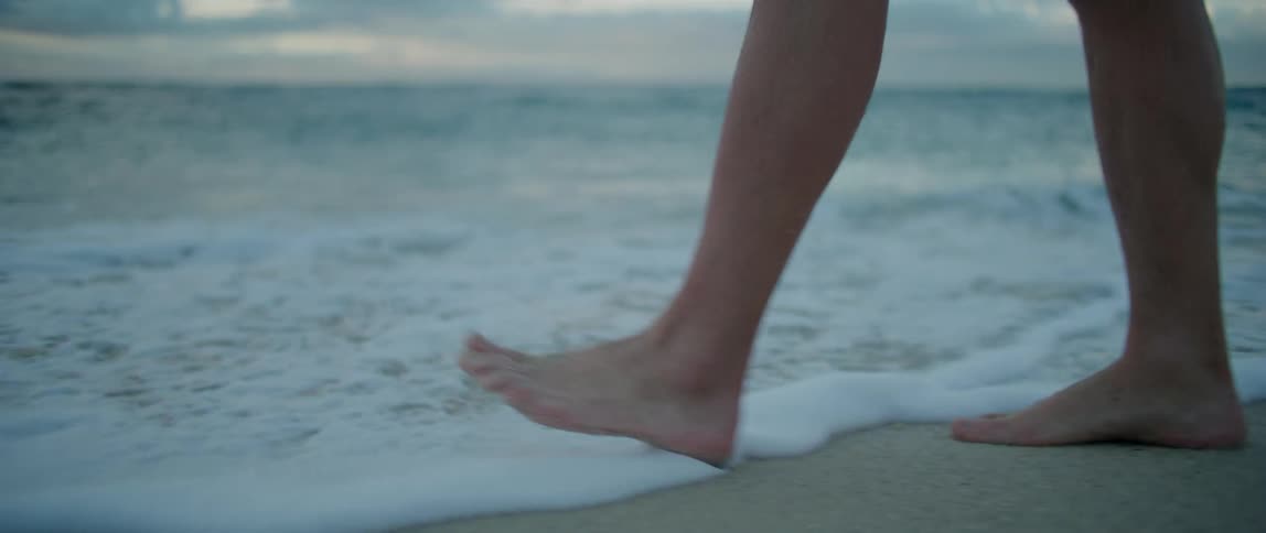 Waves wash upon a mans feet as he wades into the ocean