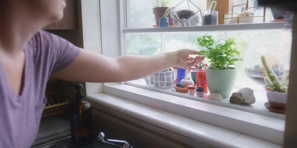 A woman leans forward to check on her small potted plants growing in her kitchen window