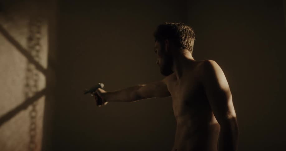 A man in a room pointing a gun with a wall in the background