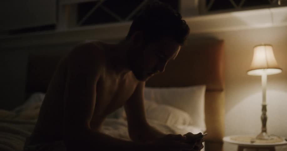 A man rushes to a nightstand to turn on the light and grab the cell phone for a phone call