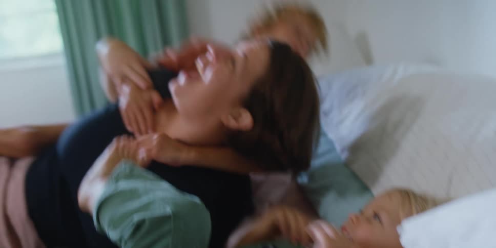 A mom plays with her children in bed