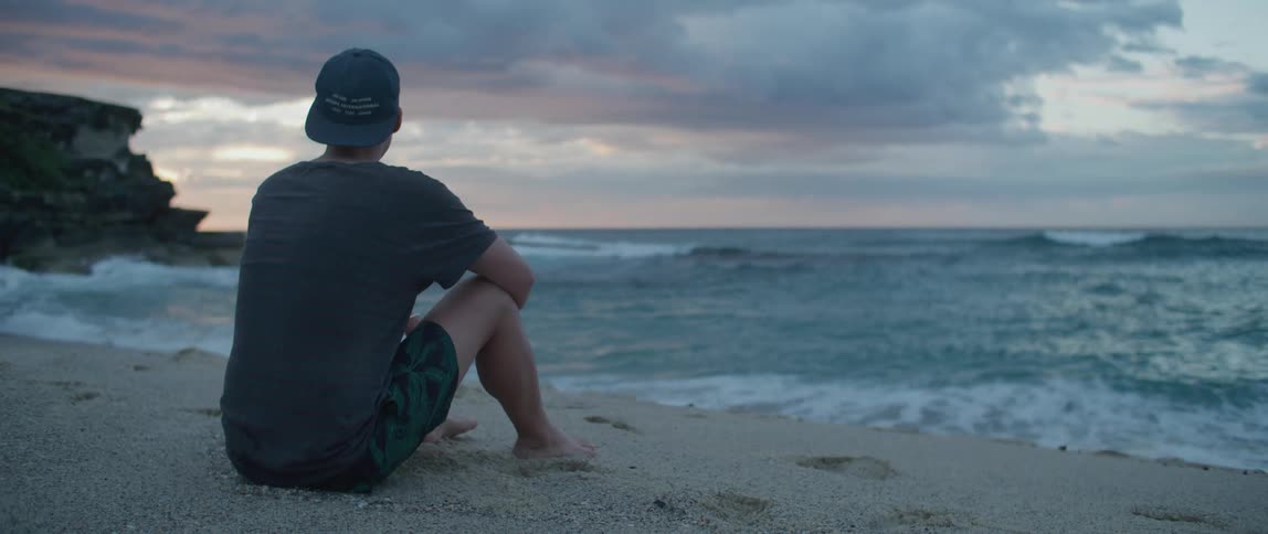 A man sits on a beach looking to the ocean water by himself