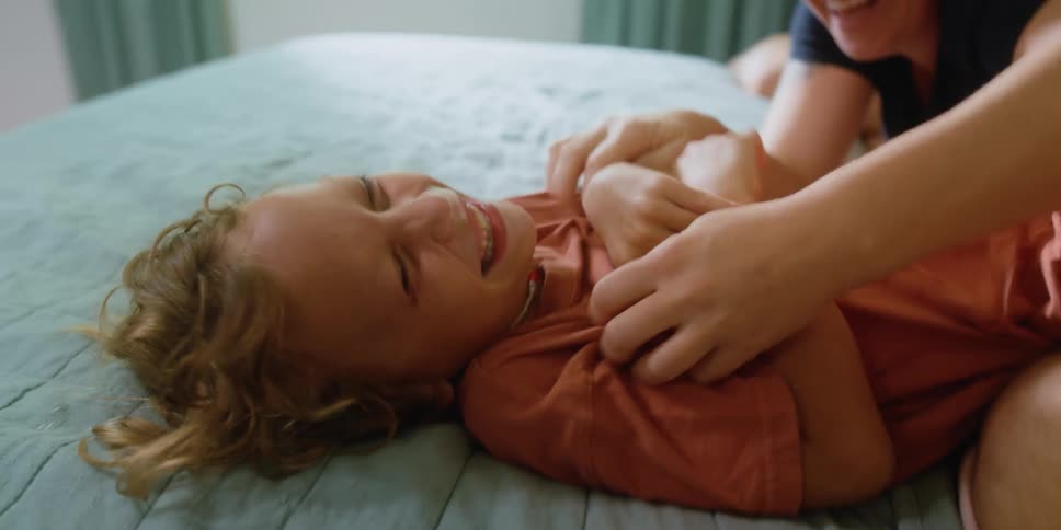 Parents tickle laughing daughter as they play together in bedroom