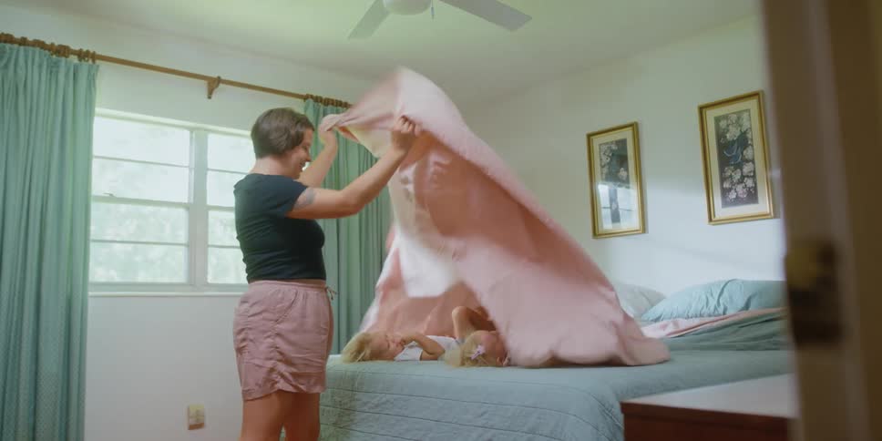 Mother uses the bed sheets to play with her children over the bed at home